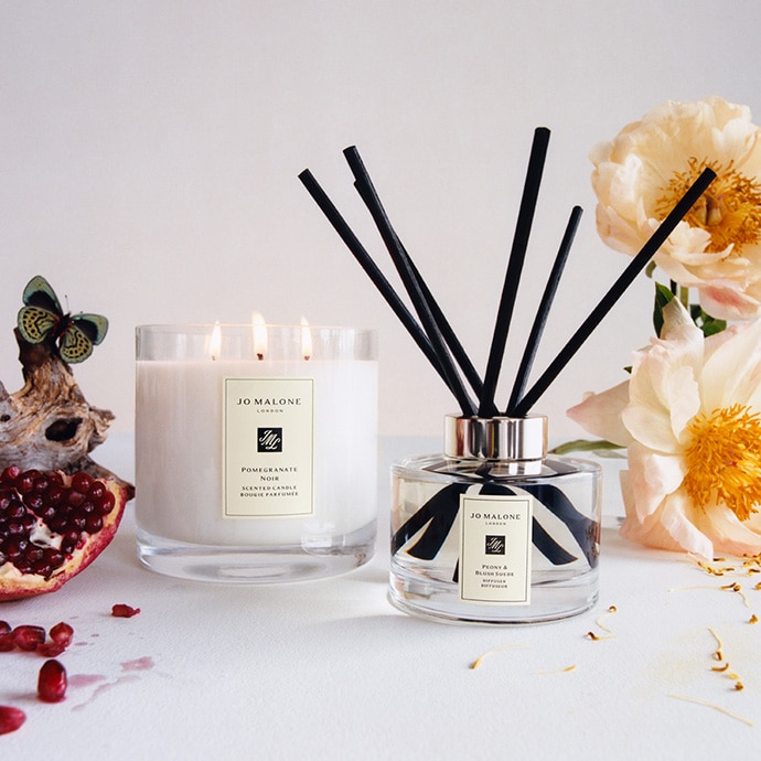 Pomegranate and Noir deluxe home candle and room diffuser surrounded by pomegranate seeds and flowers