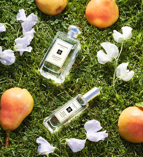 Jo Malone London English Pear Colognes on grass, surrounded by pears and sweet peas