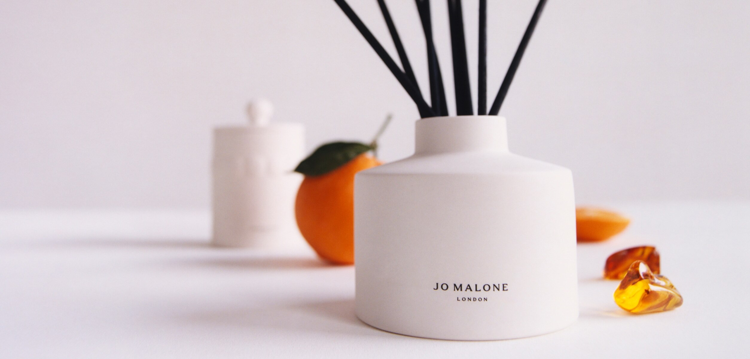 Jo Malone London white ceramic diffuser with black reeds surrounded by oranges and amber for golden amber and orange scent