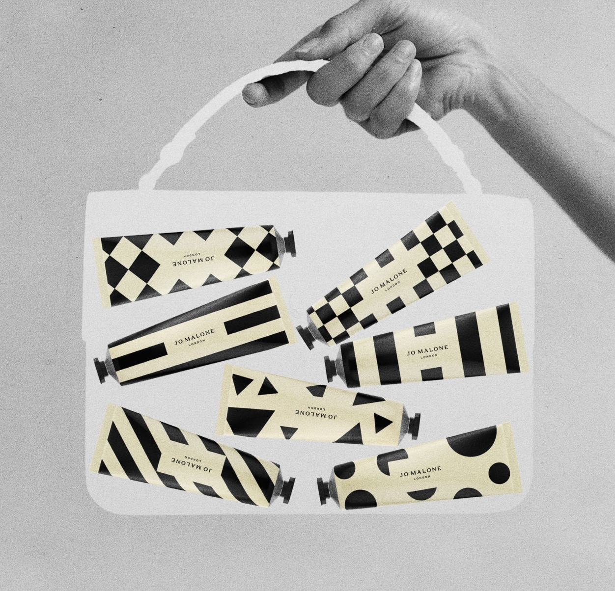 Black, white & cream image of a transparent, medium bag held by a hand, containing seven patterned hand creams in tubes.