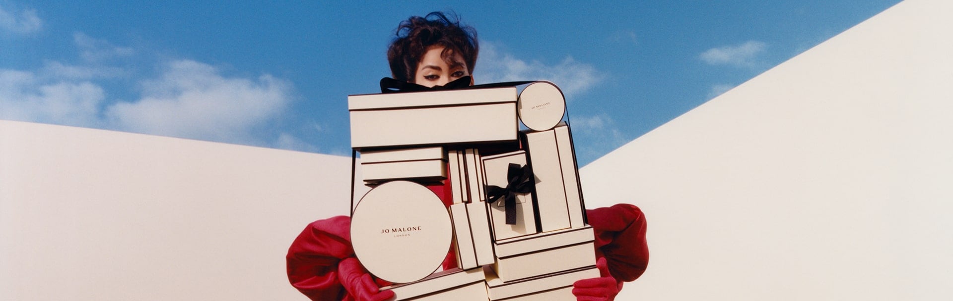 woman sitting on a hill, holding classic jo malone london black and cream gift boxes