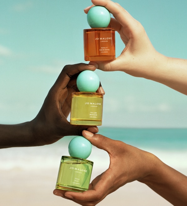Jo Malone London Blossoms Collection three colognes being held in hands with beach behind