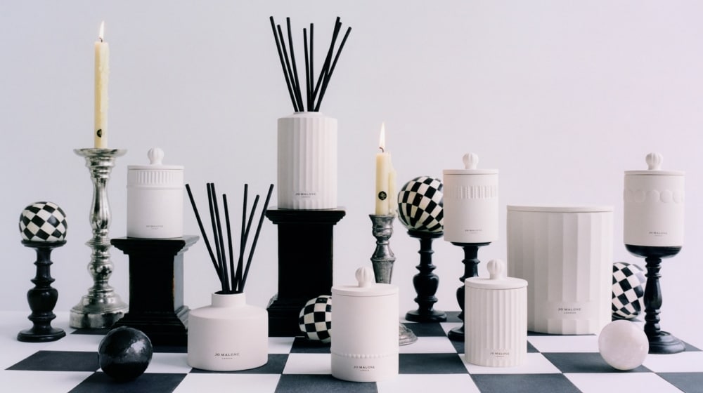 A refined arrangement of white diffusers and candles with glowing candlelight, set on a black-and-white checkered surface.
