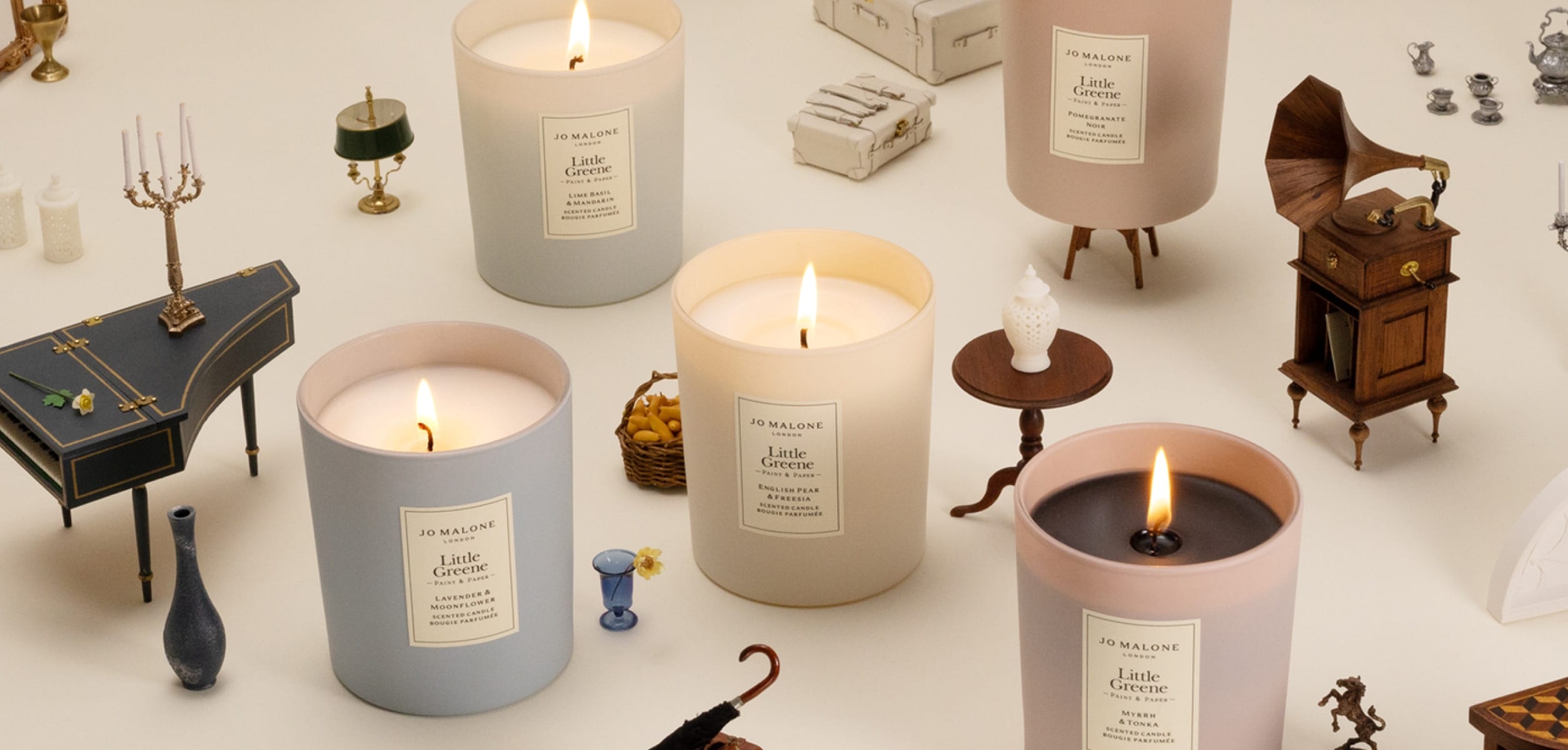Five lit candles in soft colours surrounded by tiny vintage-style furniture and props.