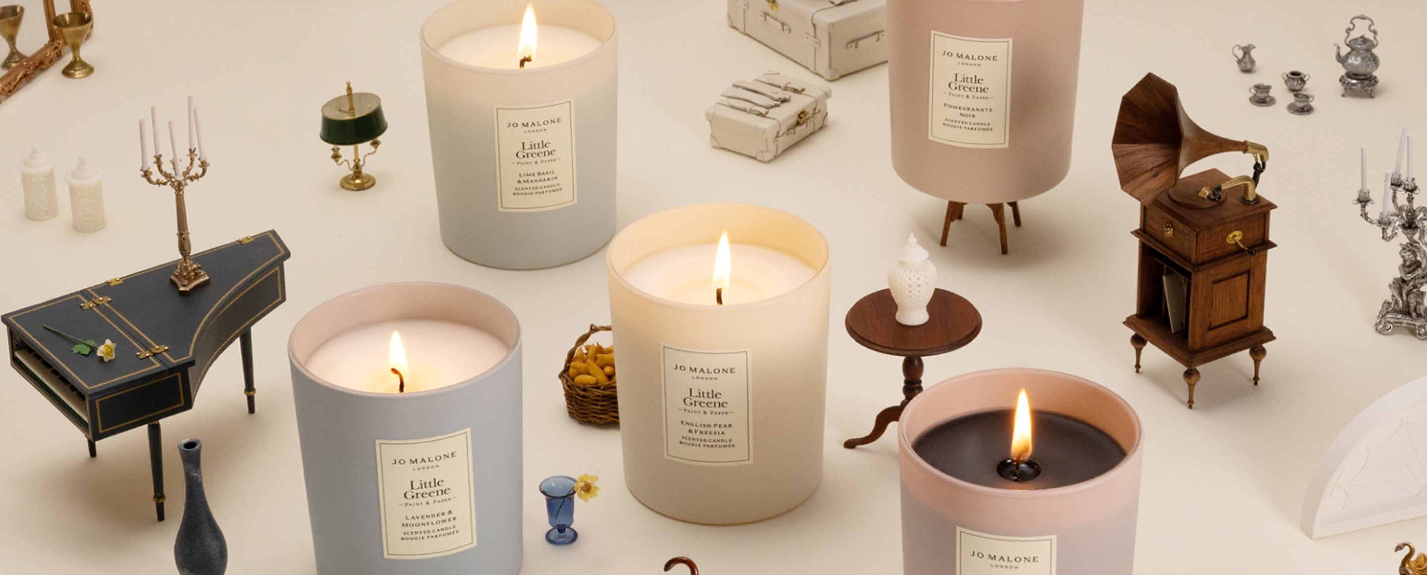 Five lit candles in soft colors surrounded by tiny vintage-style furniture and props.