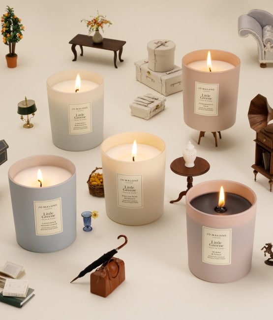 Five lit candles in soft colors surrounded by tiny vintage-style furniture and props.