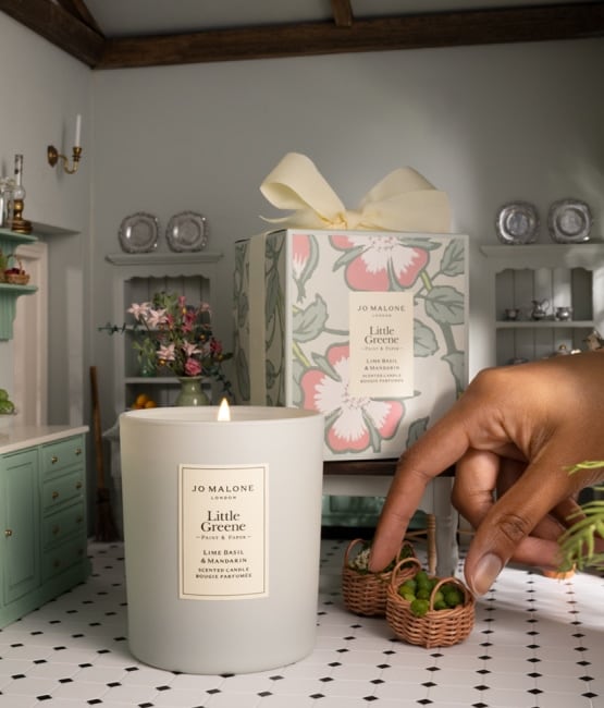 A candle in a miniature vintage kitchen as a hand places tiny baskets on the floor.