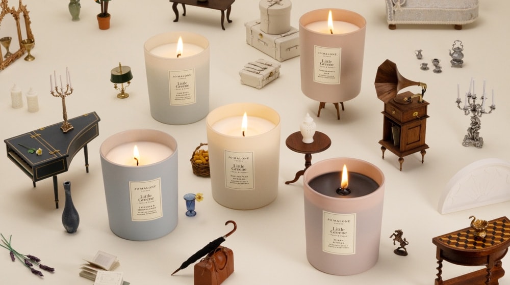 Five lit candles in soft colours surrounded by tiny vintage-style furniture and props.
