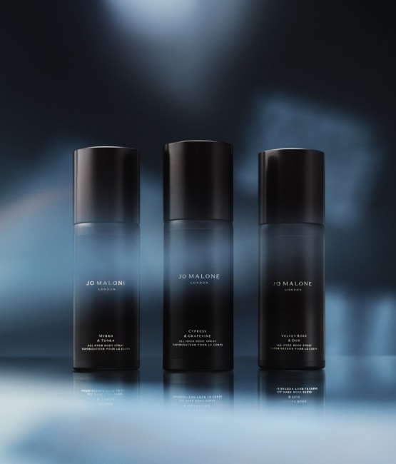 Four black Jo Malone London body spray bottles with blue light and shadows in the background.