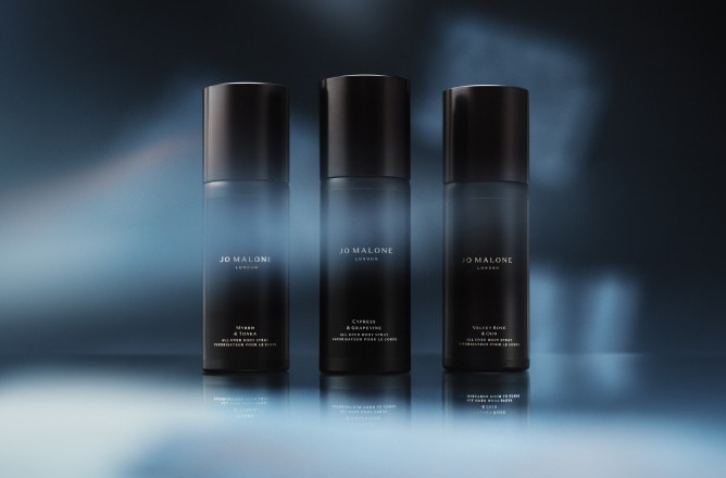 Three black Jo Malone London body spray bottles with blue light and shadows in the background.