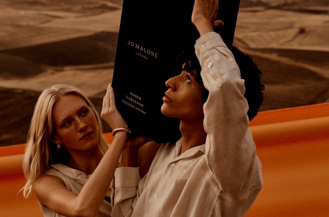 Two people in a desert holding an oversized Jo Malone London cologne bottle above their heads.