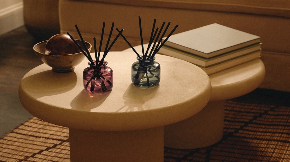 A pair of colourful refillable diffusers on a round table, styled with books and décor in a warm, neutral living room setting.