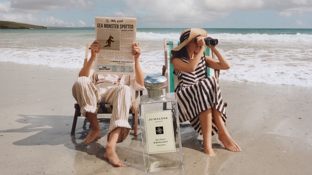Jo Malone London | Man and Women in deck chair on the beach with giant cologne bottle in front of them 