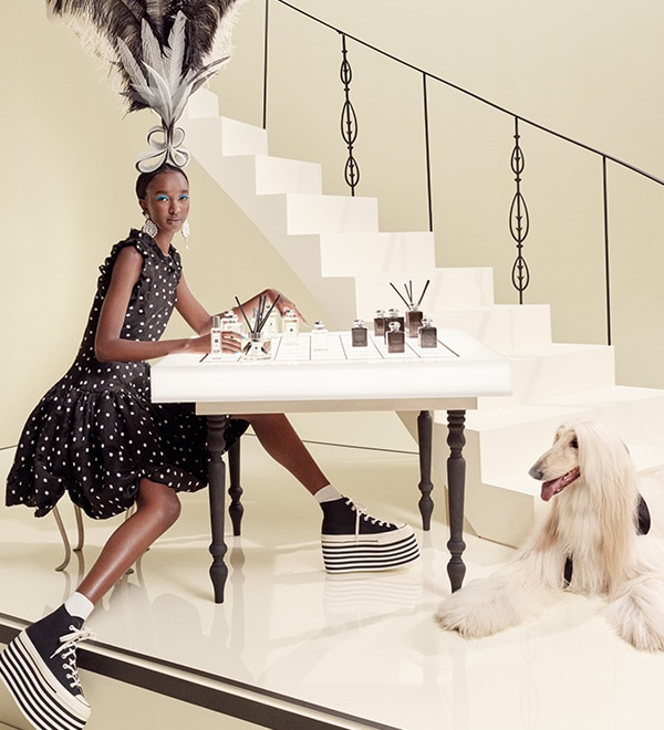 Jo Malone London woman in black dress with feathers in her hair at a table with an afghan hound