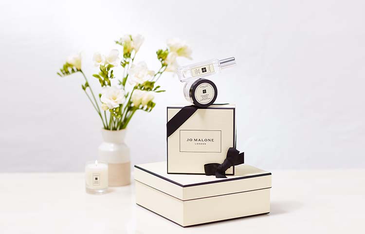 iconic jo malone london black & cream gift boxes stacked with a vase of flowers, travel candle & body creme