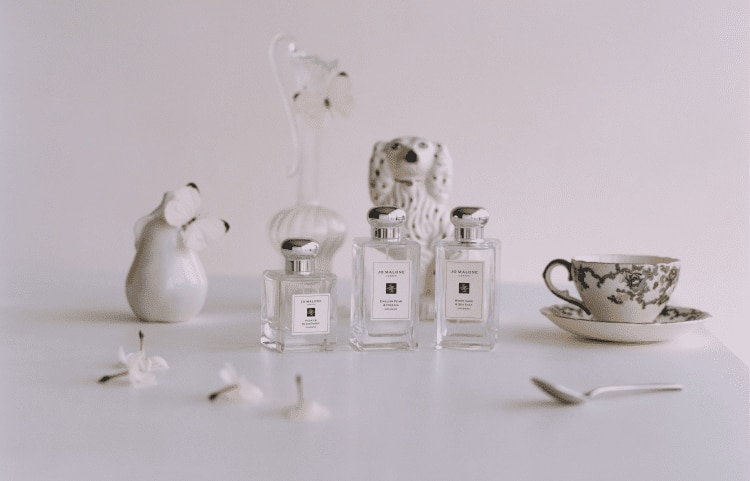 Image of three jo malone colognes in various sizes next to a teacup and a butterfly